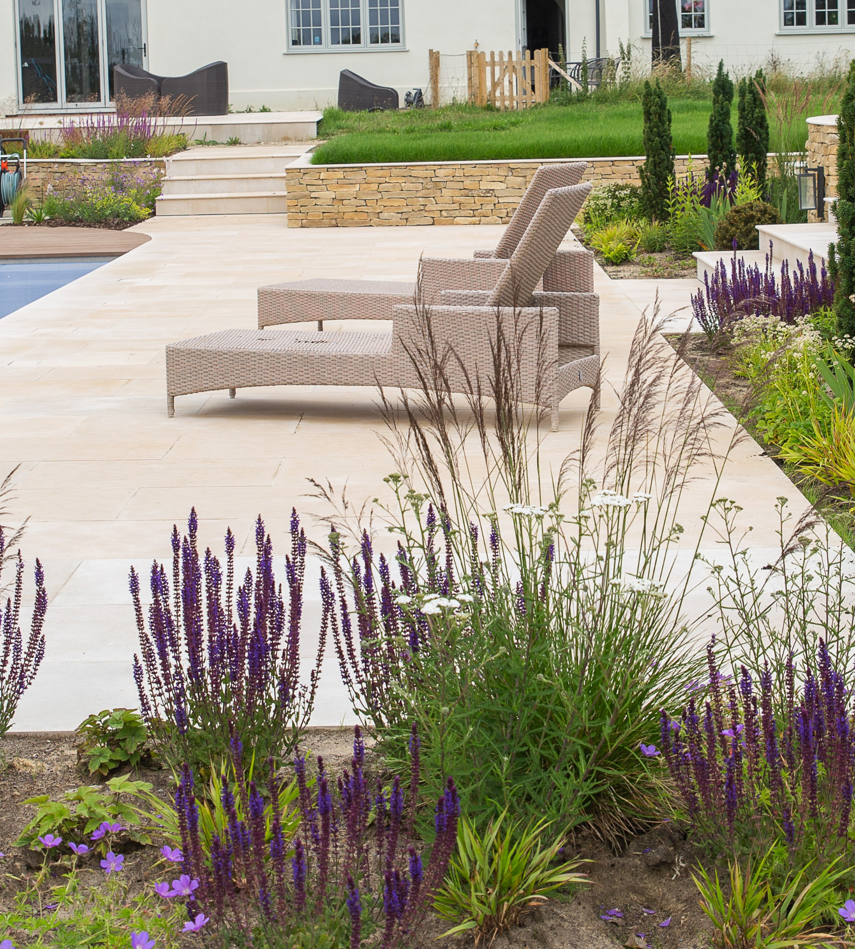 Luxury garden landscaping with a refined limestone terrace, planted borders and loungers beside a pool