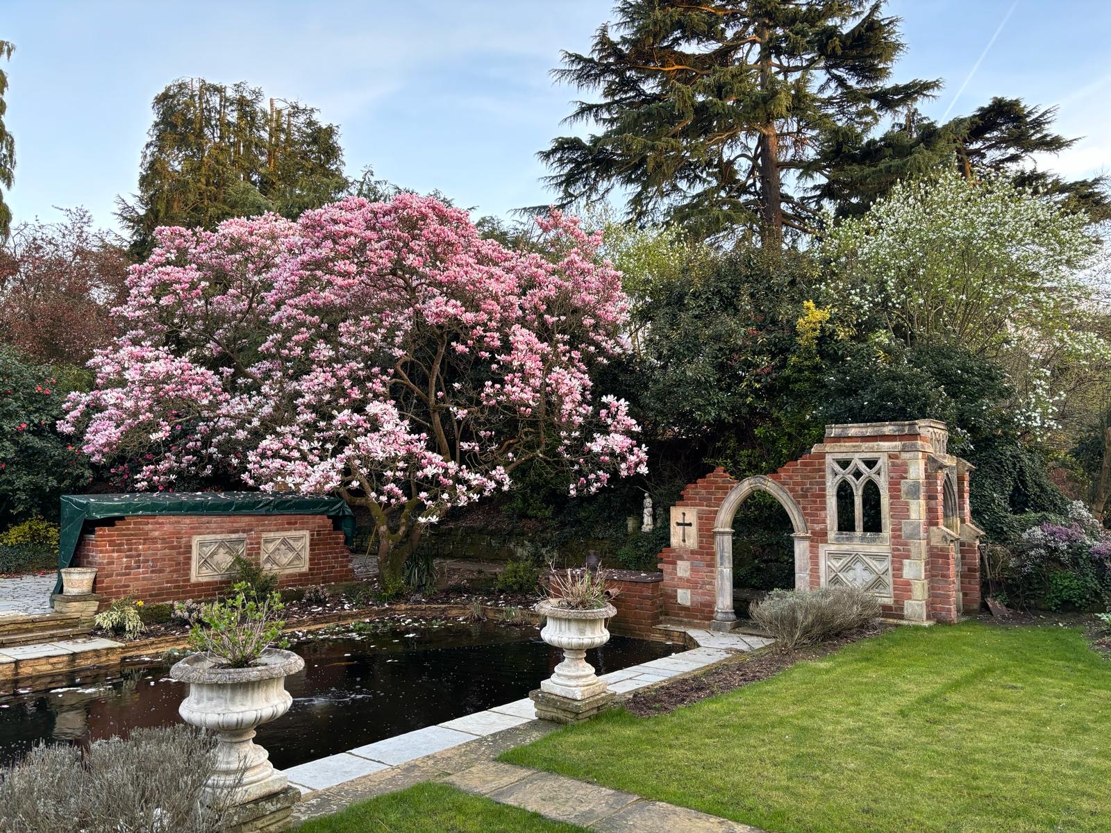 Formal garden pond with a handmade brick folly, flowering magnolia and classical stone urns