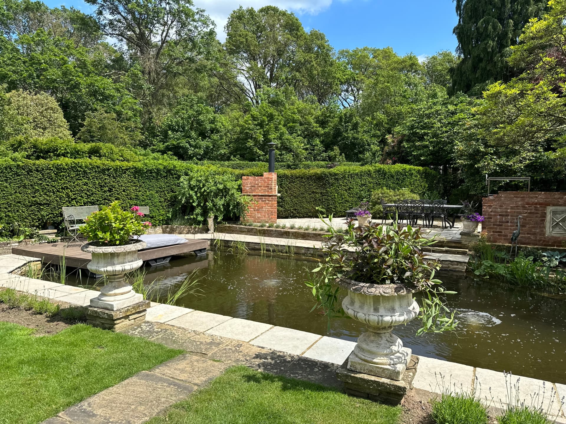 Formal luxury garden pond edged with stone paving, urns and a handmade brick feature wall