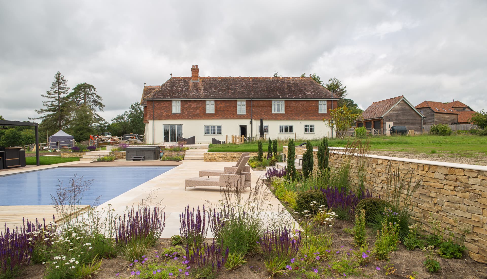 Luxury pool terrace with natural stone paving, retaining walls and loungers beside a country house